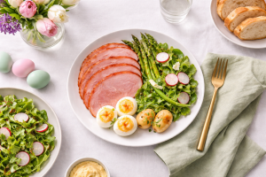 Easter brunch plate with sliced ham, deviled eggs, fresh vegetables, and spring salad in soft natural light